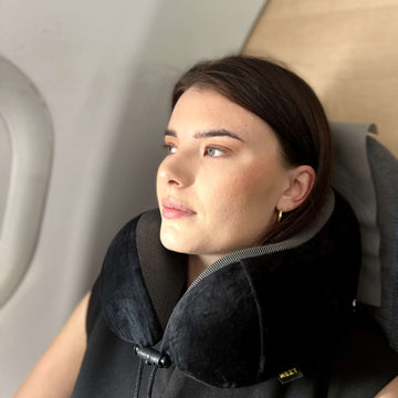 En kvinna vilar bekvämt i ett flygplanssäte, med huvudet stött av en REZT resekudde.