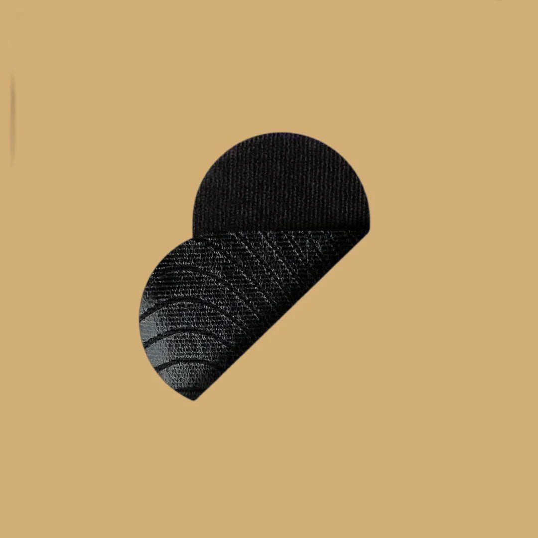 En detaljerad vy av en enskild REZT sovtejp i svart. Tejpen är böjd och visas mot en enfärgad varm beige bakgrund som matchar förpackningens färg. Tejpens textur är tydlig och ser mjuk ut.